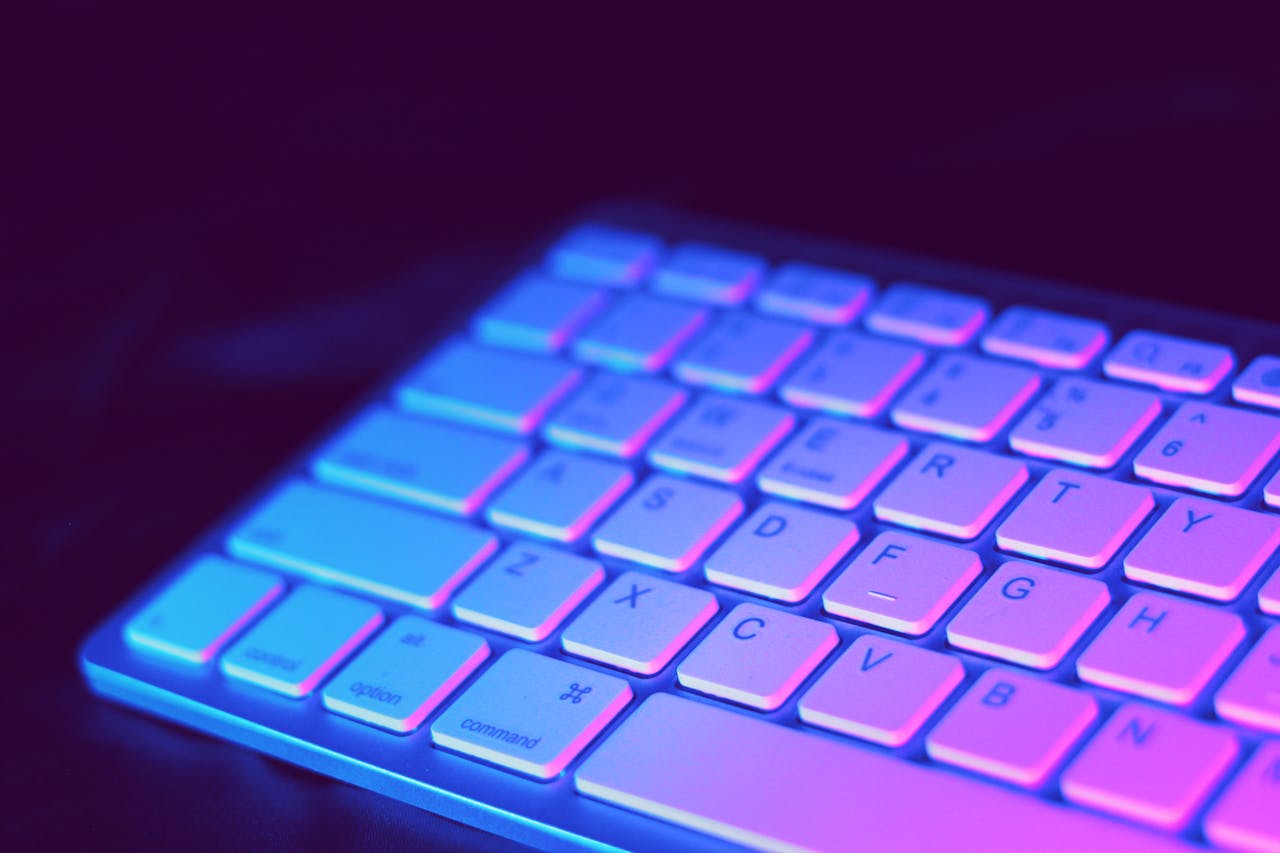 services-bg Close-up of a modern keyboard illuminated with vibrant purple and blue neon lighting.